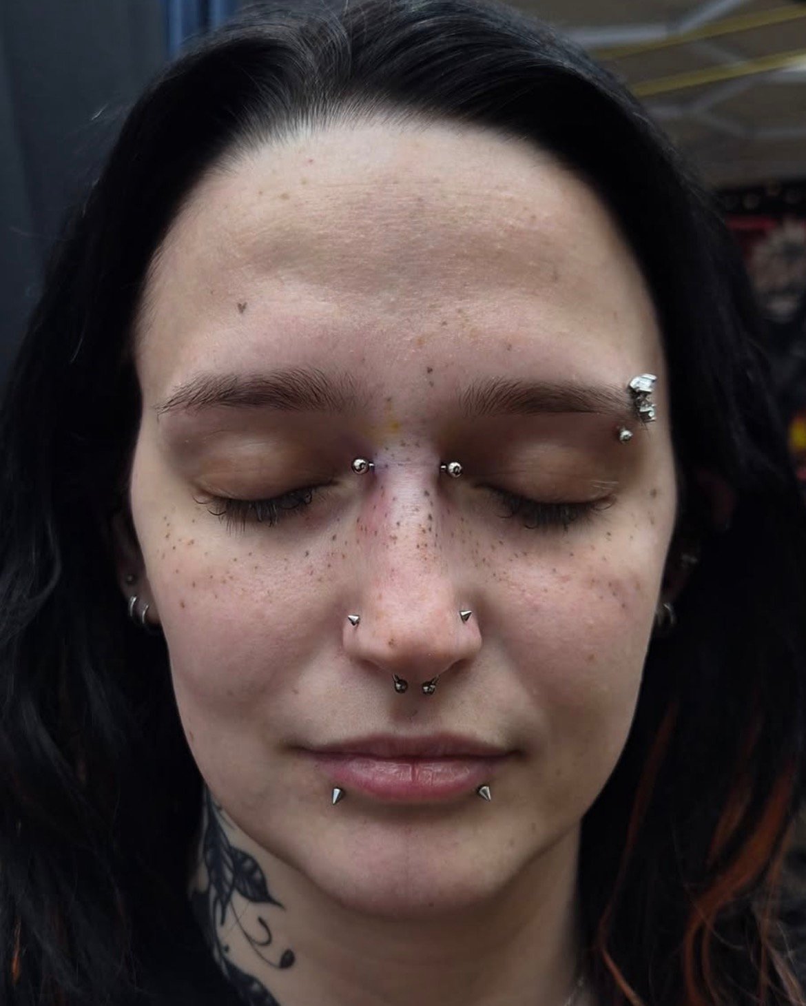 Multiple facial piercings including bridge, eyebrow, nostril, septum, and lip piercings